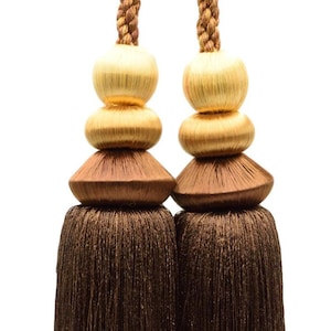 Peut inclure: Une paire de jetés de rideaux en tissu brun avec des perles dorées et brunes. Les glands sont faits d'un matériau doux et soyeux et ont un aspect luxueux.