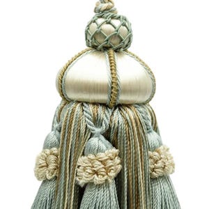 Pode incluir: Borla decorativa com um design complexo. A borla apresenta um topo bulboso creme com um detalhe de rede tecida e é acentuada com fios azul claro, bege e dourado. A parte inferior tem uma série de borlas azul claro e pompons bege.