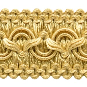 May include: A horizontal strip of gold-colored decorative trim featuring a repeating pattern of raised, braided semi-circles and leaf-like motifs. The trim has a textured, woven appearance with a consistent metallic gold finish throughout the design.