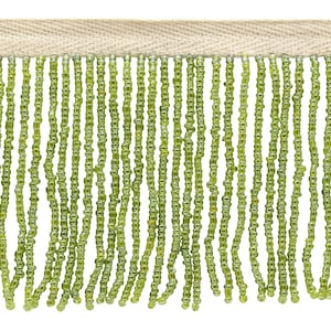 May include: Green beaded fringe trim with a beige backing. The fringe is made of small, round beads that are strung together to create a continuous strand. The backing is a solid beige fabric.