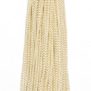 May include: A decorative tassel with a knotted top and a long, flowing fringe. The tassel is made of a light beige, woven material. The tassel is hanging against a white background.
