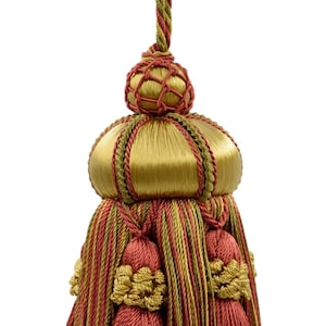 May include: A decorative tassel in gold and red. It has a braided hanging cord, a rounded top, and a fringed base. The design incorporates gold and red elements, giving it a luxurious appearance. Ideal for curtains or other decorative uses.