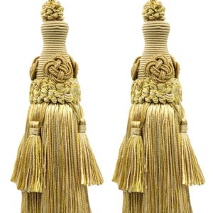 May include: Two decorative gold tassels with a knotted design and layered fringe. The tassels have a rope-like top and are made of a blend of gold and beige threads. These elegant tassels are suitable for home decor.