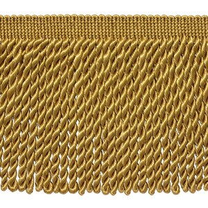 May include: Close-up of gold-colored fringe trim. The trim features a woven top edge and a series of twisted rope-like strands hanging down. The color is a warm, metallic gold, suitable for decorative purposes.