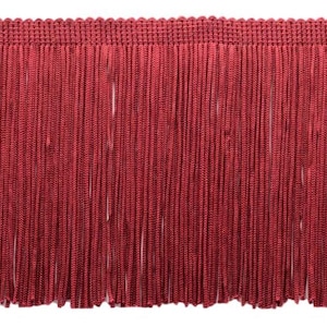 May include: A close-up shot of burgundy fringe trim. The trim has a woven top edge and long, vertical strands. The strands are evenly spaced, creating a textured, decorative element. This trim is suitable for craft and sewing projects, adding a stylish finish.