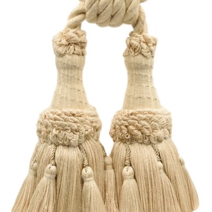 May include: A pair of cream-colored tassel tiebacks with a rope tie. The tassels have multiple layers and are made of a soft, woven fabric.