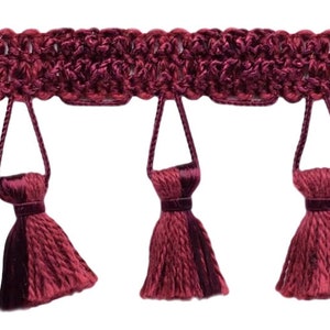 May include: Burgundy tassel trim with a woven top and fringe tassels. The trim is approximately 2.5 cm wide.