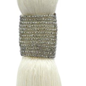May include: White tassel curtain tieback with a silver beaded trim. The tieback is made of a thick, braided rope.