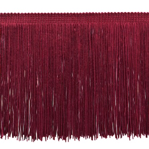 May include: A close-up of a burgundy fringe trim. The trim has a woven top edge and a dense, vertical fringe of long, thin strands. The colour is a deep, rich red, suitable for craft and design projects.
