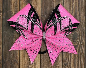 May include: A pink and black cheer bow with a geometric design and silver glitter. The bow is decorated with rhinestones.