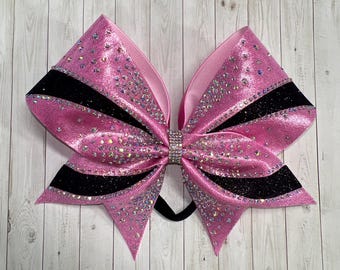 May include: A pink and black cheer bow with rhinestones. The bow has a black velvet ribbon with pink stripes.