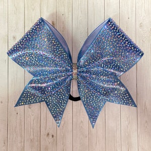 May include: A large blue cheer bow with iridescent rhinestones. The bow is made of a soft, sparkly fabric and has a classic cheer bow shape.