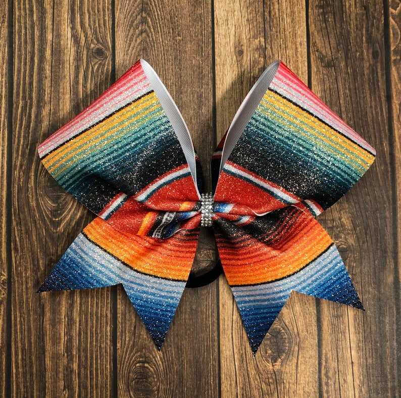 May include: A large, colorful bow with a red, orange, blue, and green striped pattern. The bow has a sparkly finish and a single rhinestone in the center.