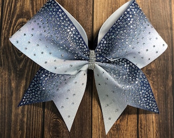 May include: A large white and navy blue cheer bow with a gradient of blue to white. The bow is covered in rhinestones.