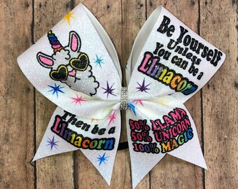 May include: White cheer bow with a glitter finish. The bow features a cartoon llama wearing sunglasses and a unicorn horn. The text on the bow reads "Be Yourself Unless You Can Be A Limacorn" and "Then Be A Limacorn 50% Llama 50% Unicorn 100% Magic".