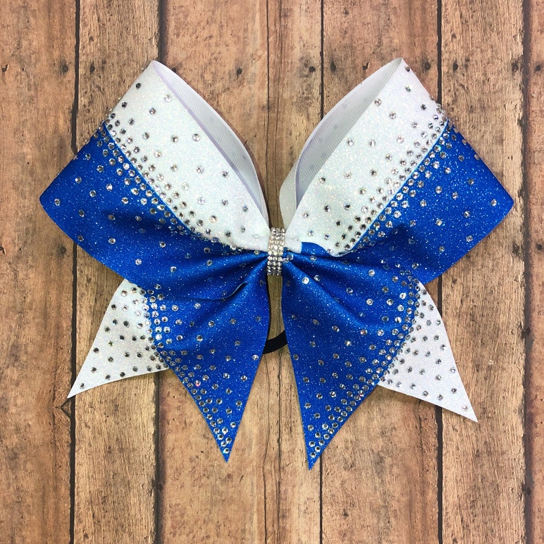 May include: A large blue and white cheer bow with silver glitter and rhinestones. The bow is tied with a black ribbon.