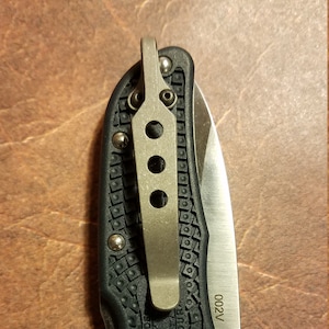 May include: A black folding knife with a silver blade and pocket clip. The knife has a textured handle with the word "SPYDERCO ENDURA" embossed. The blade has the text "002V" and a circular hole.