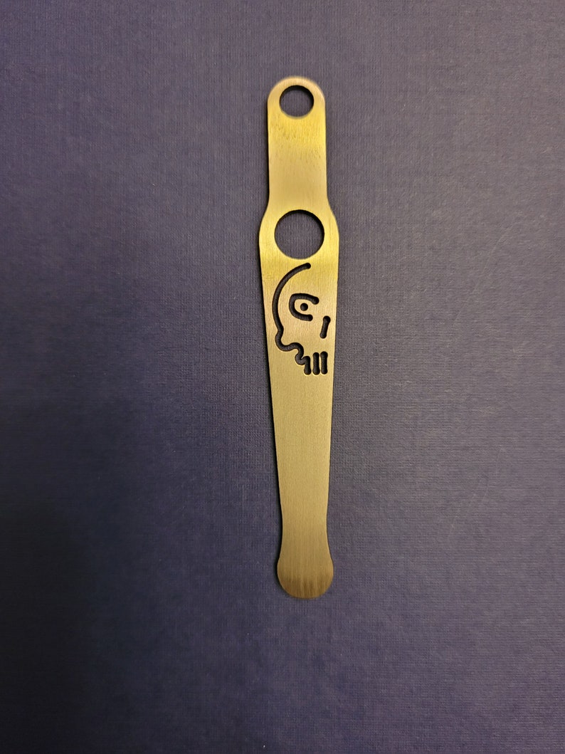 May include: A gold metal bottle opener with a skull design. The opener has a hole at the top for hanging and a small hole near the bottom for opening bottles.