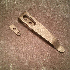 May include: A silver pocket clip with a rounded end and three holes. A smaller silver piece with two holes is also included.
