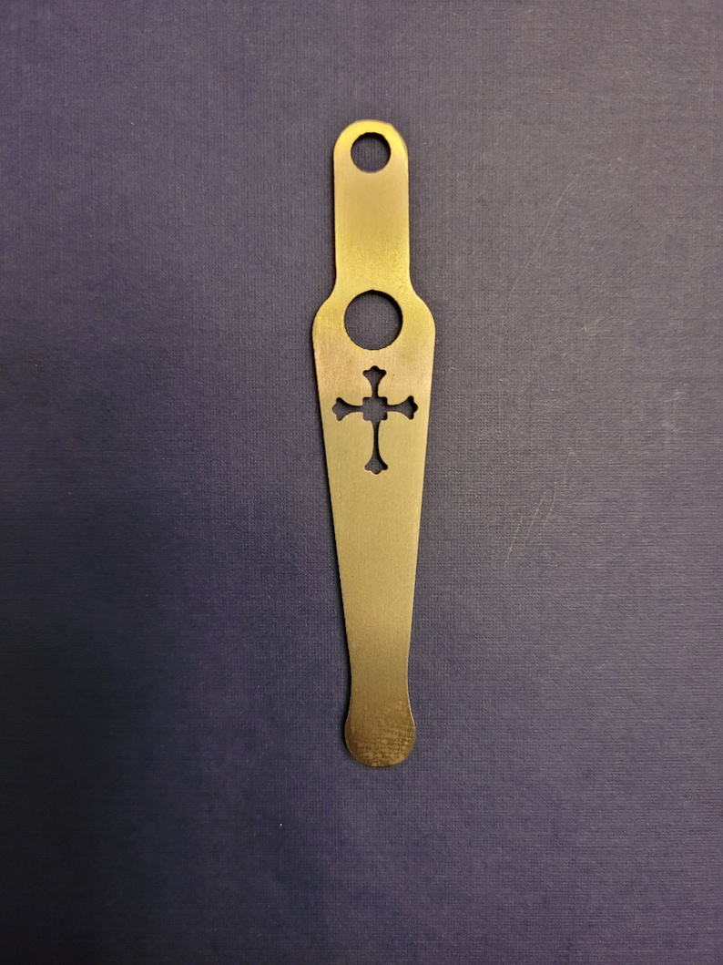 May include: A gold metal bottle opener with a cross-shaped cutout. The opener has a hole at the top for hanging.