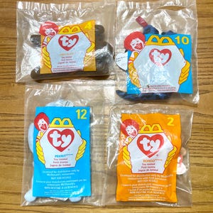 May include: Four sealed McDonald's Ty Beanie Baby toys. The toys are in clear plastic bags with colorful cardboard packaging. The packaging features the Ty logo, Ronald McDonald, and the names of the toys: Chocolate, Peanut, Bongo, and another toy.