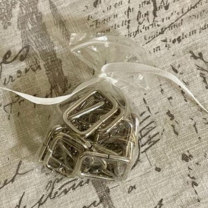 May include: A clear plastic bag filled with silver metal D-rings. The bag is tied with a white ribbon.