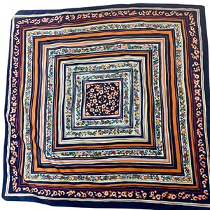 May include: Square silk scarf with a repeating floral and geometric pattern. The scarf features a navy blue border, orange stripes, and a central square with a floral design in shades of pink, green, and yellow.