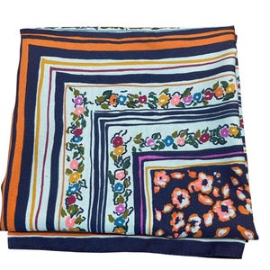 May include: Folded square scarf with a floral and striped pattern. The scarf features a navy blue border with orange and white stripes. The center has a white background with colorful flowers and a navy blue square.