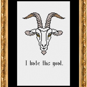 May include: Cross-stitch artwork of a goat's head with horns, eyes, and beard, framed in gold. The text "I hate this goat" is below the goat image. The artwork is on a white background.