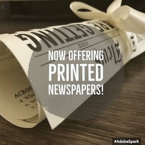 May include: A rolled up newspaper with a white ribbon tied around it. The newspaper has the text "FREE" and "NOW OFFERING PRINTED NEWSPAPERS!" on it. The image has the hashtag #AdobeSpark.