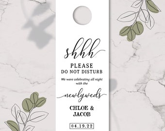 May include: White door hanger with a black cursive text that says "shhh please do not disturb we were celebrating all night with the newlyweds Chloe & Jacob 04.19.22".