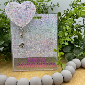 May include: A white iridescent badge holder with a silver retractable badge reel and a heart-shaped charm. The badge holder has the text "Chaos Coordinator" printed on it.