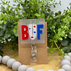 May include: A clear glitter badge holder with a red, white, and blue "BUF" design. The holder is attached to a retractable badge reel with a clear plastic strap.