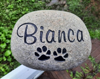 May include: A gray stone with the name "Bianca" engraved in black lettering. Two black paw prints are also engraved on the stone.