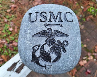 May include: A gray stone with the USMC logo and the words "USMC" engraved in black.