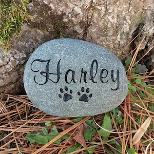 May include: A gray stone with the name "Harley" engraved in cursive lettering and two paw prints.