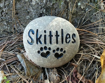 May include: A gray stone with the name "Skittles" engraved on it. Two black paw prints with hearts are also engraved on the stone.