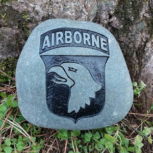 May include: A gray stone with a black and white image of the 101st Airborne Division insignia, including the words "AIRBORNE" above the eagle.