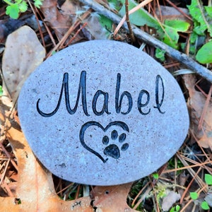 May include: A gray stone with the name "Mabel" engraved on it. A heart with a paw print is engraved below the name.