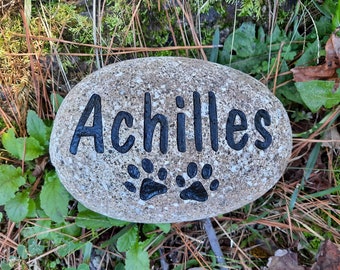 May include: A gray stone with the name "Achilles" engraved in black lettering. Two black paw prints are below the name.