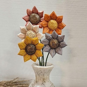 May include: A set of five carved wooden flowers in shades of yellow, orange, cream, pink, and grey, each with a textured center. The flowers are arranged in a small, off-white vase with a crackled, distressed finish and a narrow neck.
