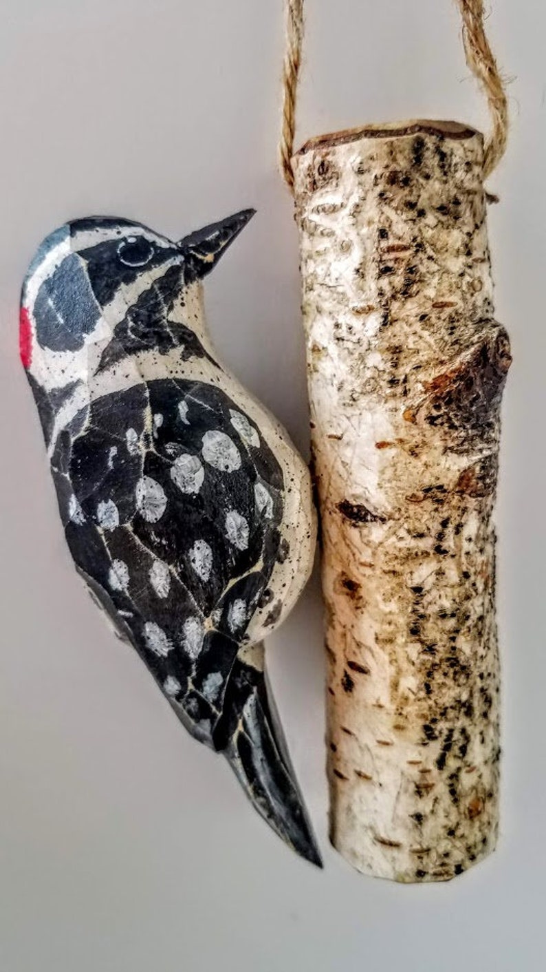 May include: A wooden bird ornament with black and white markings and a red beak, hanging from a birch bark log ornament.