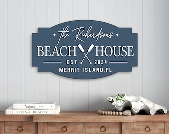 May include: A blue wooden sign with white text that reads "The Richardsons Beach House Est. 2024 Merritt Island, FL". The sign has a white image of two crossed oars.