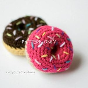 Könnte beinhalten: Zwei gehäkelte Donuts, einer pink mit bunten Streuseln und einer braun mit weißen Streuseln. Die Donuts liegen auf einem weißen Hintergrund. "PATTERN ONLY" steht auf den Donuts.