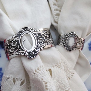 May include: Two silver napkin rings with an ornate design. The larger ring has a cutout in the shape of the letter "O".