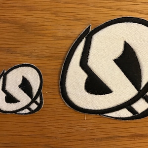 May include: Two white and black embroidered patches featuring the logo of the Pokemon,  Gengar. The larger patch is approximately 3 inches in diameter and the smaller patch is approximately 1.5 inches in diameter.