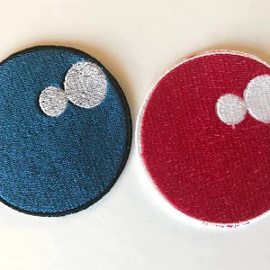 Könnte beinhalten: Zwei runde, gestickte Aufnäher mit weißen Kreisen auf blauem und rotem Hintergrund. Die Aufnäher haben einen Durchmesser von etwa 5 cm.
