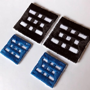Puede incluir: Cuatro parches bordados de forma cuadrada. Dos son negros con detalles blancos y dos son azules con detalles blancos. Los parches tienen un diseño tejido, con un patrón de líneas horizontales y verticales.