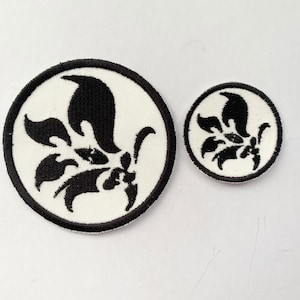 May include: Two circular patches with a floral design. The patches feature a white background with a black floral design in the center. A black border surrounds the white background. One patch is larger than the other.