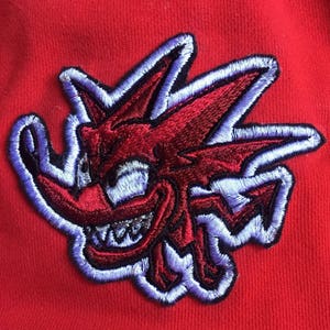 May include: Red and purple embroidered patch of a cartoon monster with a spiky head and a wide grin.